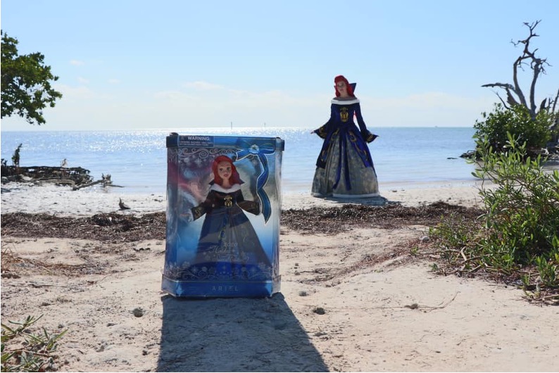 Christina dressed as Christmas Ariel on a beach in the background with the Christmas Ariel Doll in the Foreground